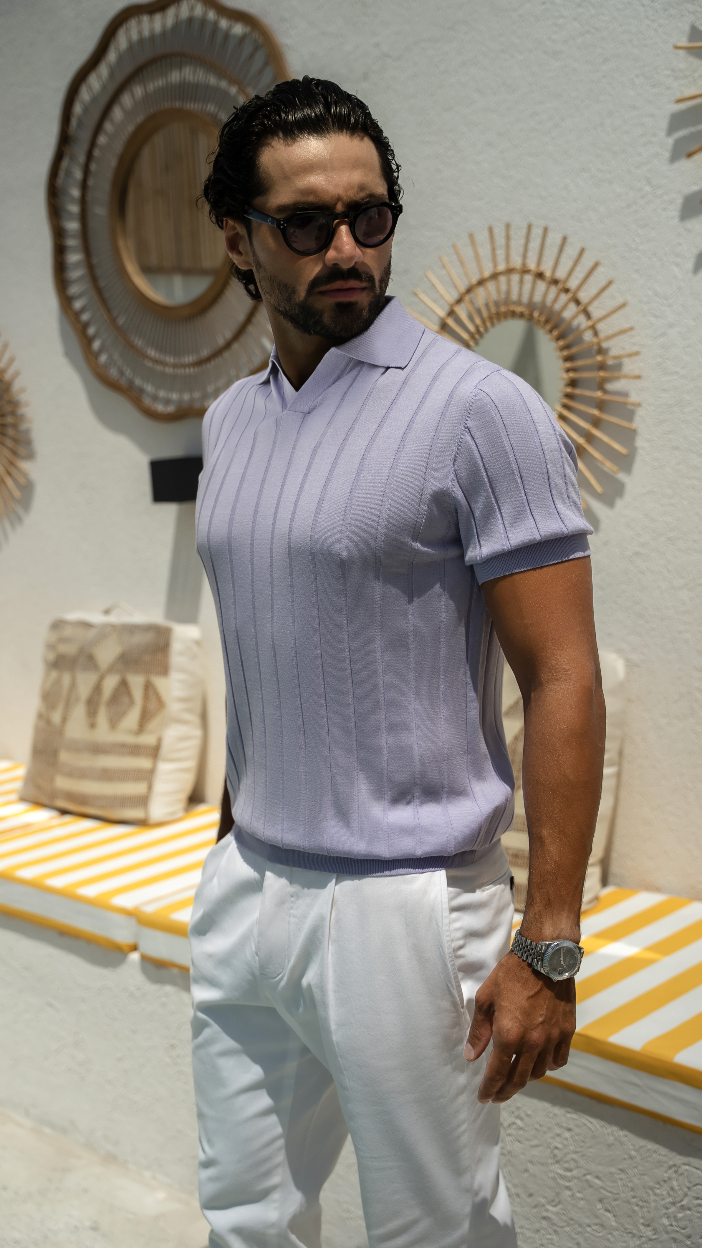 A man wearing a lilac knitted polo shirt with white shorts, standing in front of a display with decorative items.
